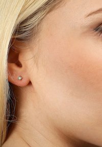 Goldfarbene Ohrstecker mit einem klaren, rund geformten Edelstein. Der Edelstein verfügt über eine facettierte Oberfläche, die seine Lichtreflexion verstärkt.