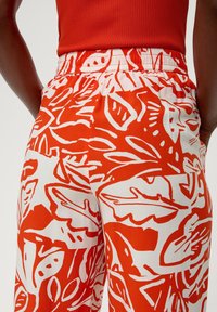 Röda och vita mönstrade byxor med bladdesign, elastisk midja och sidofickor. Tyget verkar lätt och texturerat.