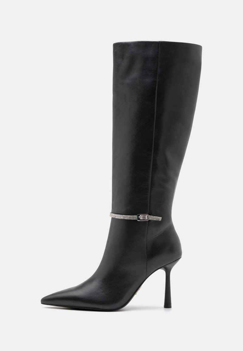Botte en cuir noir à hauteur de genou avec un bout pointu et un talon aiguille haut. Présente une sangle décorative en argent autour de la cheville. Texture lisse.