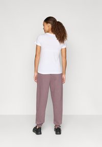 Biela tričko s krátkym rukávom skombinované so voľnými, svetlofialovými teplákmi a čiernymi teniskami, pohľad zozadu.