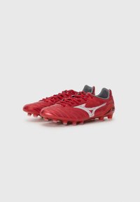 Rode synthetische voetbalschoenen met grijze accenten, een gestructureerd oppervlak en gevormde noppen voor grip. Bevat een opvallend zilveren logo aan de zijkant.