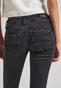 Pantalones vaqueros negros de mezclilla con diseño ajustado, que presentan una cintura de altura media, bolsillos traseros estilizados y una sutil textura deslavada.