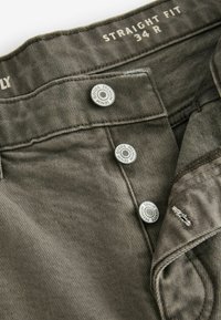 Gerade geschnittene Hose aus olivgrünem Textilgewebe mit silbernen Metallknöpfen und Nähdetails, gekennzeichnet mit dem Etikett "34 R" am Bund.