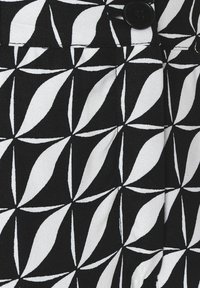 Tissu noir et blanc présentant un motif géométrique de formes interconnectées avec une finition texturée et un détail en bouton noir.
