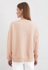 Hellrosa übergroßes Sweatshirt mit Rundhalsausschnitt, überschnittenen Schultern und gerippten Bündchen. Glatte Textur, minimalistisches Design, keine sichtbaren Logos.