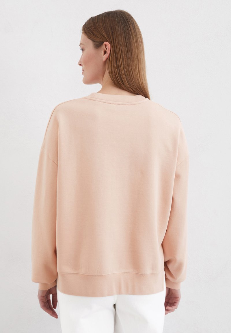 Jasnoróżowy, oversize sweatshirt z okrągłym dekoltem, opadającymi ramionami i ściągaczami. Gładka tekstura, minimalistyczny design, brak widocznych logo.