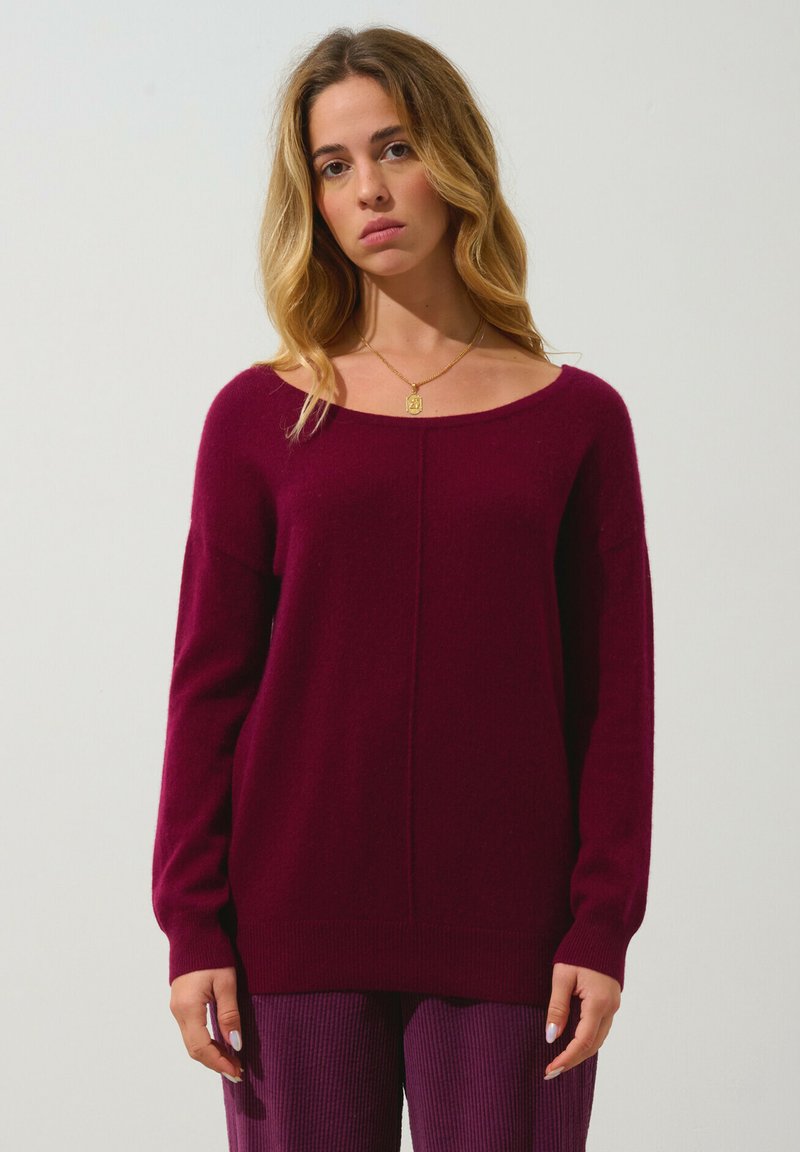 Burgunderröd stickad tröja med vid halsringning och långa ärmar, med en enkel design och mjuk textur, i kombination med randiga lila byxor.