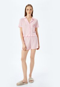 Conjunto de pijama rosa de manga corta que incluye una camisa de botones con un diseño bordado, acompañada de pantalones cortos a juego. Tejido suave y texturizado.