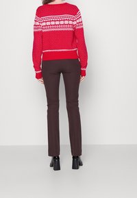 Pull en tricot rouge avec des motifs de flocons de neige blancs et de pois, associé à un pantalon marron ajusté et des chaussures à talons carrés noires.