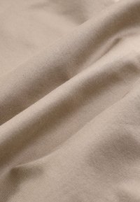 Gros plan d'un tissu beige lisse avec une texture fine tricotée visible et des plis doux soulignant la douceur et la flexibilité.