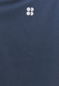 Marineblått tyg med en subtil ribbad struktur som har en liten, vit logotyp i det övre vänstra hörnet.