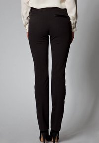 Slim-fit black trousers with a smooth texture, subtle sheen, and a back pocket accent near the waistband. Worn with high heels.