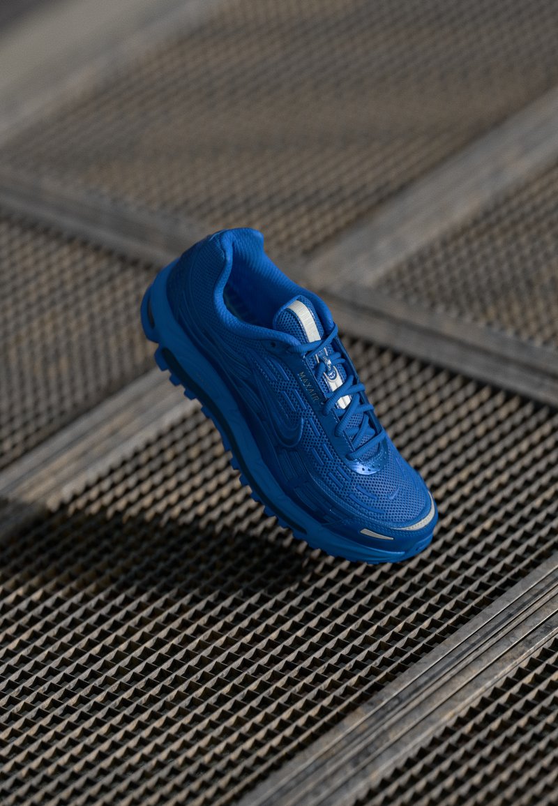 Blue athletic shoe with textured upper, lace-up design, and reinforced toe cap. Lightweight sole and prominent branding detail.