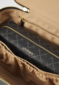 Black textured pouch with gold zipper, inside a beige fabric-lined bag. The pouch features a patterned exterior and a visible logo.
