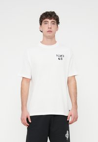 Λευκό βαμβακερό t-shirt με κοντά μανίκια και στρογγυλή λαιμόκοψη, με μαύρο γραφικό σχέδιο στην αριστερή πλευρά του στήθους. Ευθεία κοπή, άνετη γραμμή.