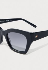 Mustad musta raami prillid, millel on halli gradient-läätsed ja väike Tommy Hilfiger logo templipoolsel käel.