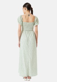 Lang grøn kjole med smocked liv og pufærmer. Blomsterprint med beige accenter. Lige kant, der når anklerne.