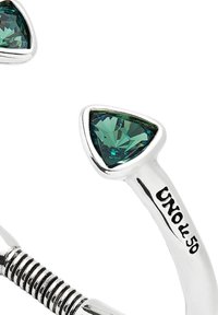 Anillo de plata con dos piedras preciosas verdes en forma de triángulo. La banda tiene una textura ligeramente estriada con un diseño en espiral. Marcado "UNO de 50."