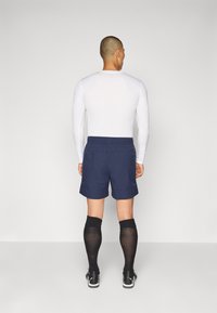 Shorts bleu marine avec une taille élastique, associés à un haut ajusté à manches longues blanc et des chaussettes noires montantes. Tissu lisse, design décontracté.