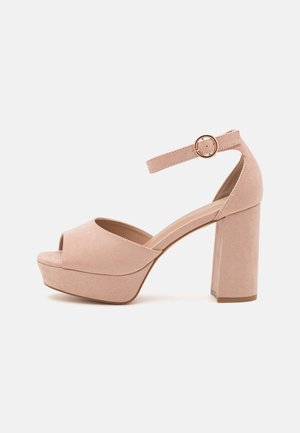 Beige ruskind platform sandal med chunky høj hæl og ankelrem med rund guldbøjle, åben tå design.