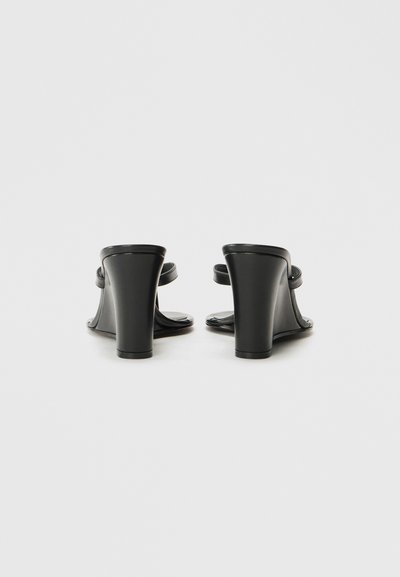 Sandales noires à talons avec deux fines lanières et un talon épais. Matériau lisse avec une finition brillante. Design à dos ouvert pour un enfilage facile.