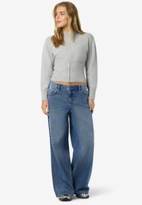 Suéter gris corto con cremallera frontal y textura acanalada, combinado con jeans de mezclilla azul de corte holgado y zapatillas grises.