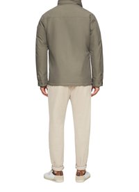 Olivgrüne Steppjacke mit hohem Kragen, softem Material und Druckknopfmanschetten; kombiniert mit beigen Cordhosen und weißen Sneakers.