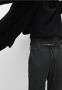 Felpa nera con scollo rotondo, abbinata a pantaloni grigio scuro a righe sottili con cintura regolabile a coulisse.