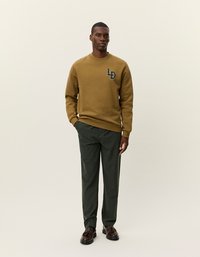 Sweatshirt vert olive à col rond et logo brodé, associé à un pantalon texturé gris foncé et des chaussures noires.