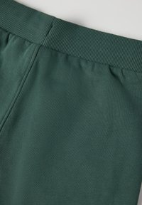 Tummanvihreä puuvillasekoitekangas, jossa on ribbireunallinen elastinen vyötärö, sisältäen sileän pinnan ja ommellut saumat.