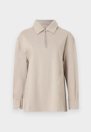 Μπεζ μακρυμάνικο πουκάμισο με μυτερό γιακά και ένα κουμπί στο λαιμό που δημιουργεί ένα μικρό άνοιγμα σε σχήμα κλειδιού.