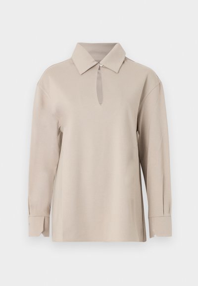 Μπεζ μακρυμάνικο πουκάμισο με μυτερό γιακά και ένα κουμπί στο λαιμό που δημιουργεί ένα μικρό άνοιγμα σε σχήμα κλειδιού.