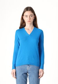 Pulover cu decolteu în V, cu mâneci lungi, de culoare albastru aprins, realizat dintr-un material moale, cu tiv și manșete cu model în bucle; purtat cu blugi de culoare albastru deschis.