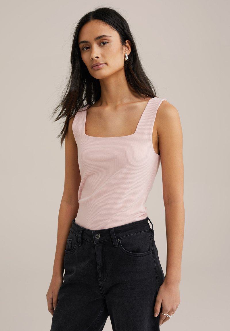 Top de tirantes de canalé rosa claro con escote cuadrado, combinado con jeans negros de cintura alta. Diseño sencillo, textura suave y acentos mínimos.