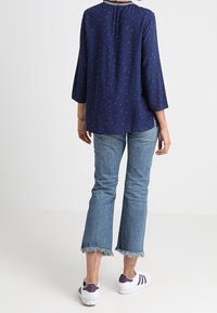 Top blu navy con piccoli pois rossi e maniche a tre quarti, abbinato a jeans svasati celesti con orli sfrangiati e sneaker bianche.