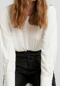Witte blouse met lange mouwen, een gladde textuur en knoopmanchetten, gecombineerd met hoge zwarte broek met een knoopsluiting.