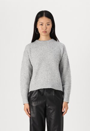 Pulover tricotat texturat de culoare gri deschis, cu guler rotund și manșete ribbate, asortat cu pantaloni din piele negri.