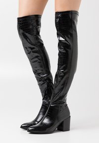 Czarne buty z sztucznej skóry za kolano o fakturze krokodylej, z wysmukłymi czubkami i blokowym obcasem. Błyszczące wykończenie podkreśla design.