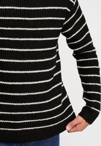 Czarnobiały sweter w paski z dzianiny, z długimi rękawami, ściągaczami na mankietach oraz luźnym krojem. Miękka tekstura z kontrastującymi poziomymi paskami.
