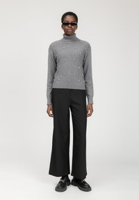 Maglione grigio con collo alto, caratterizzato da un motivo a diamante e perle decorative. Abbinato a pantaloni neri a gamba larga e scarpe nere chunky.