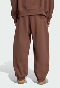 Bruna sweatpants i mjukt tyg, med en lös passform, elastiska muddar och en vid silhuett, tillsammans med beige skor.