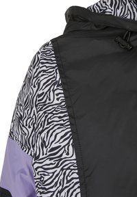 Crna jakna sa zebra uzorkom u bijeloj i crnoj boji, s lavandom akcentima. Glatka tekstura i detalj sa podešavanjem kapuljače.