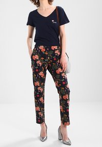 Námořnický tričko s V-čelním výstřihem a výšivkou "LOVE", kombinované s přiléhavými černými kalhotami s květinovým vzorem v oranžové, růžové a zelené. Stříbrné podpatky.