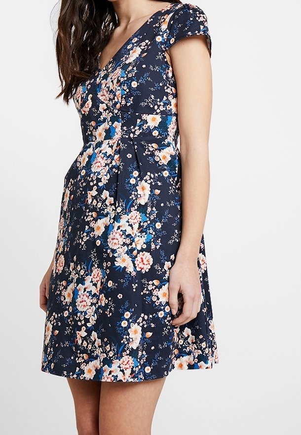 Femme portant une robe à manches courtes florale bleu marine avec un décolleté en V et une jupe évasée.