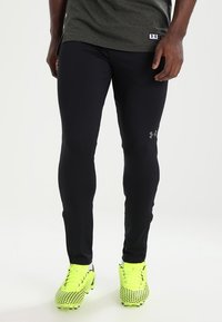 Černé sportovní legíny s obepnutým střihem a reflexními detaily loga. V kombinaci se světlými žlutými kopačkami s texturovaným vzorem.