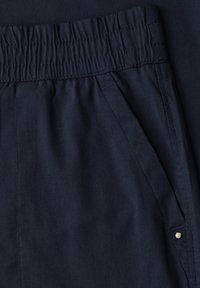 Close-up of navy blue pants with elastic waistband and angled front pocket with a small metal button detail.