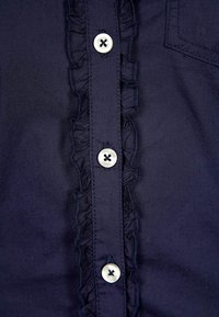 Camicia blu navy con un plissé, caratterizzata da bottoni argentati con centro nero e una piccola tasca sul lato sinistro.
