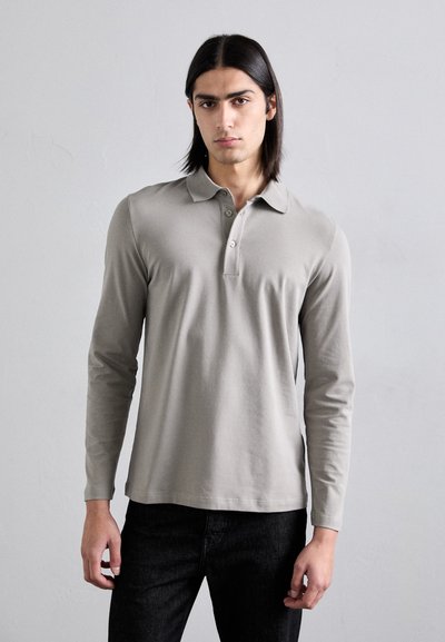 Cămașă polo cu mânecă lungă din bumbac gri deschis. Prezentă o guler și o închidere cu trei nasturi. Purtați-o cu blugi skinny negri. Design simplu, textură moale.