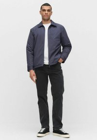 Marinblå bomberjacka med dragkedja, med en bröstficka och platt krage, kombinerad med svarta jeans och svarta sneakers.