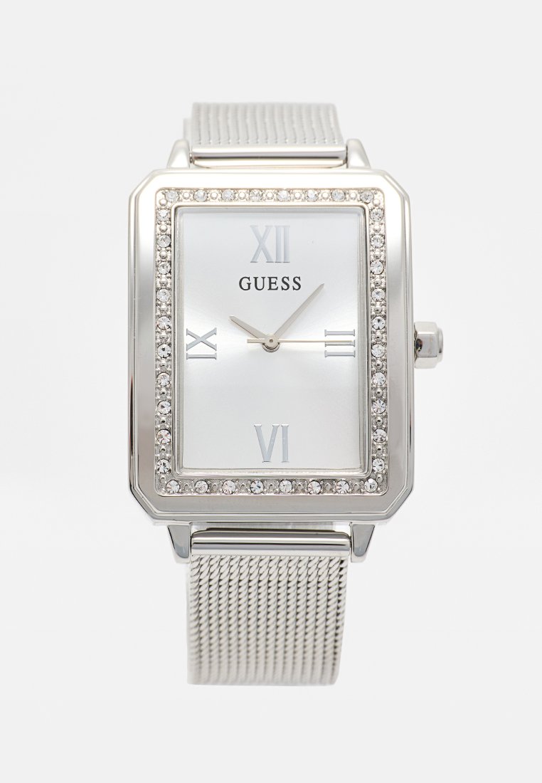 Reloj de pulsera Guess rectangular plateado con bisel decorado con cristales, esfera blanca, números romanos en 12, 3, 6 y 9, y correa de malla metálica.
